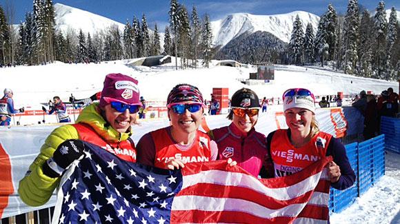  	 Kikkan Randall, Holly Brooks, Liz Stephen and Jessie Diggins wave the flag to cheer on their teammates in the team sprint at the Laura Cross Country Center outside Sochi. (USSA-Margo Christiansen)